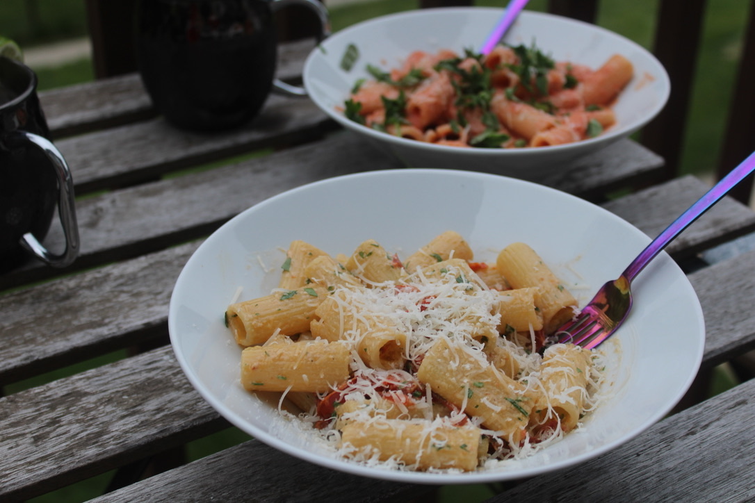 two different pasta dishes on a table, with two mugs slightly out of frame