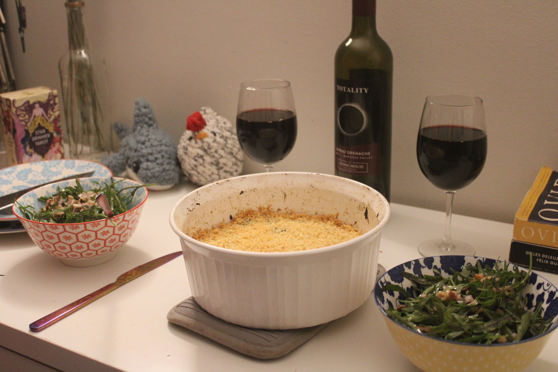 a gratin dish on a potholder, with an eggplant gratin, next to two salads in bowls